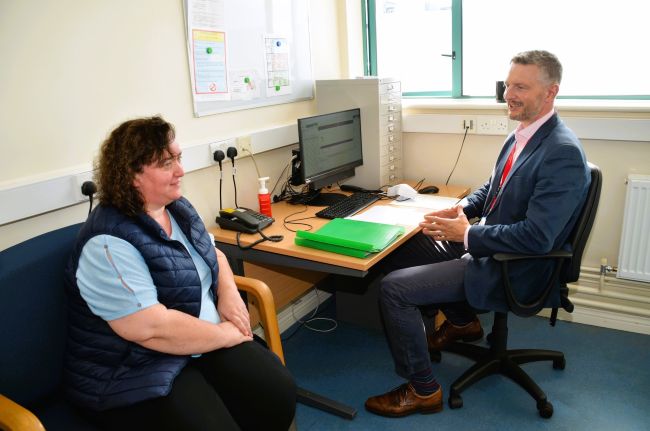 A doctor and a woman sitting at a desk during a consultation.